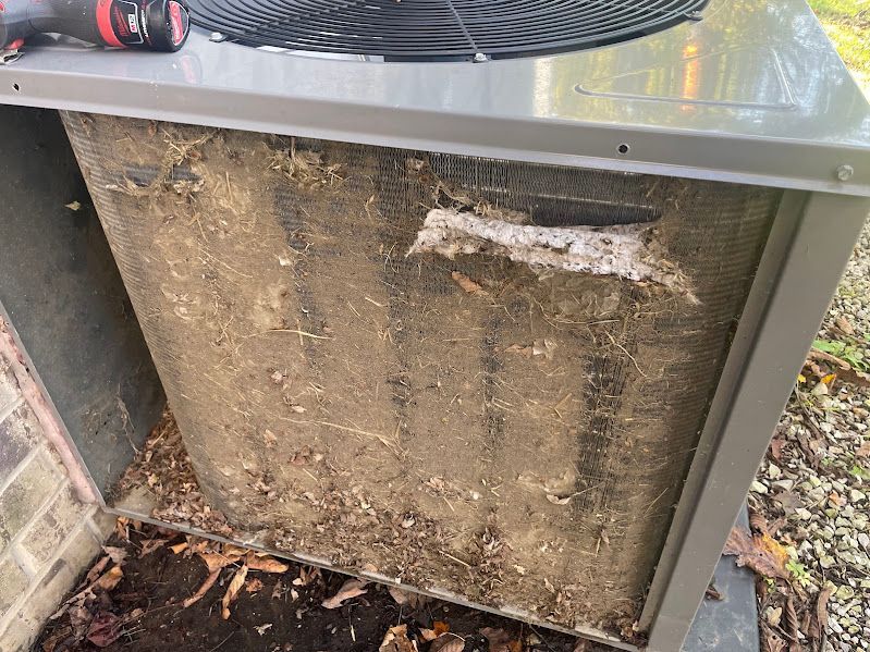 Dirty outdoor HVAC unit with mud caked on the front panel and a damaged, torn area near the top.