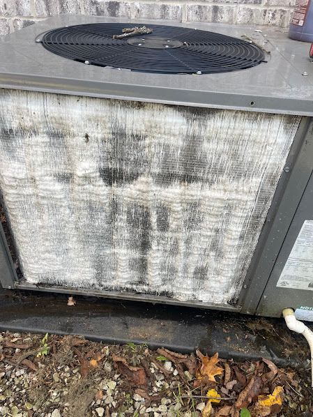 Dirty outdoor air conditioner unit with a heavily stained front grille and leaves on the ground nearby
