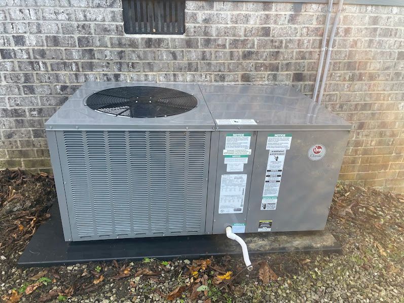 Outdoor HVAC unit beside a brick wall, with a fan on top and white pipes connected at the front.