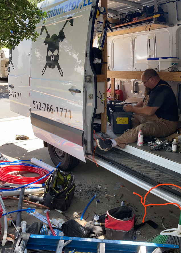 Technician working inside a service van with tools and coiled hoses spread on the ground outside.