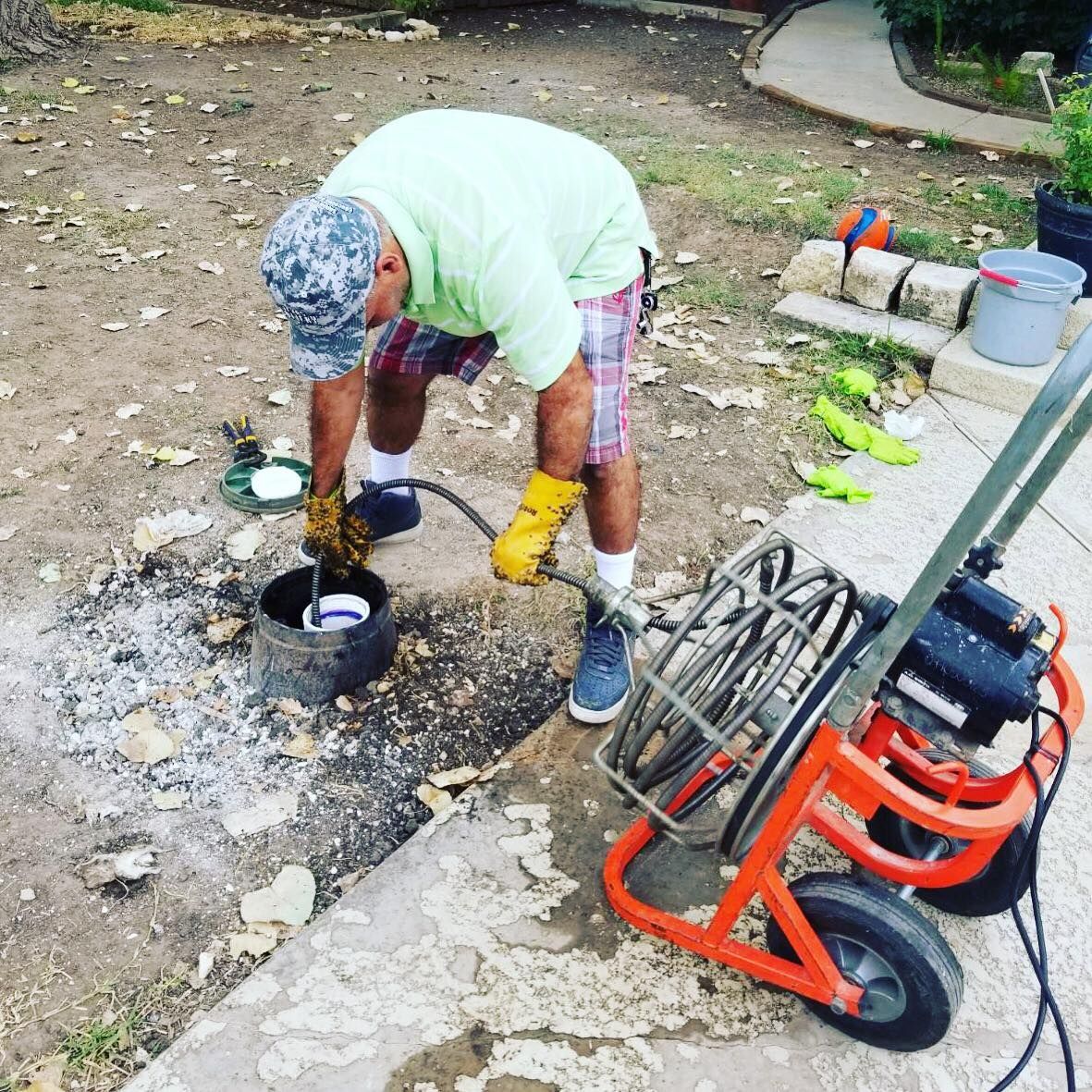 Person in green shirt and yellow gloves working outdoors beside a portable pressure washer and hose reel.