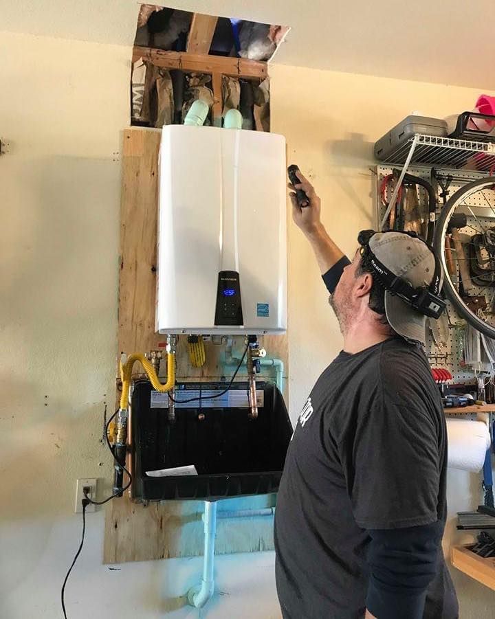 Man inspecting a wall-mounted boiler with exposed piping in a garage or workshop