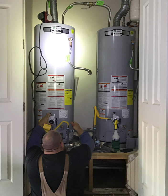 Worker servicing two water heaters in a narrow utility closet