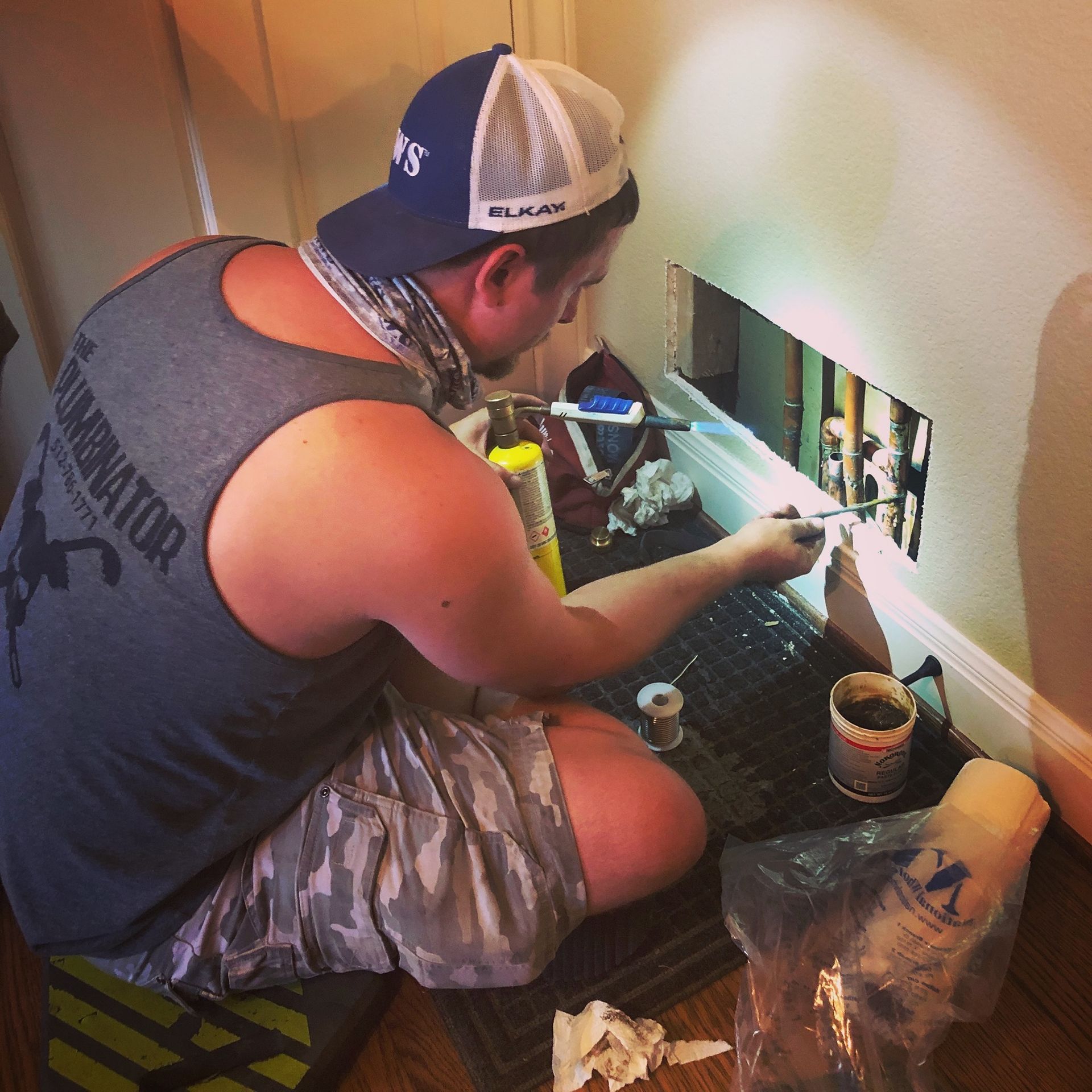 Man kneeling by a wall opening, working on plumbing with tools and supplies nearby