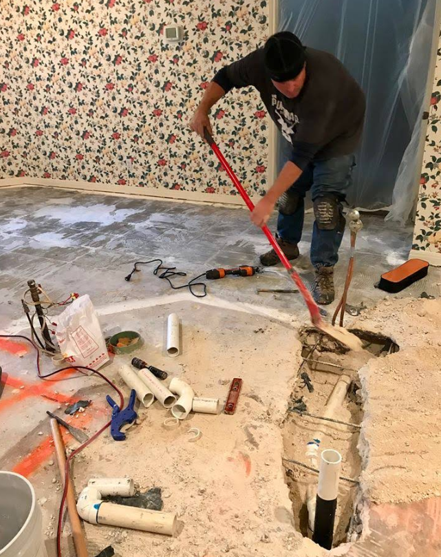 Worker using a red pry bar to break up a floor slab during home renovation