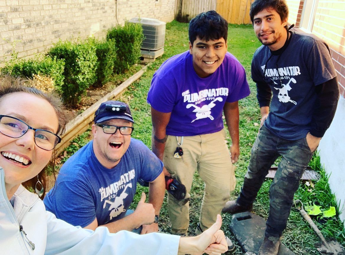 Four smiling people outdoors, posing together on a patio with a garden behind them.