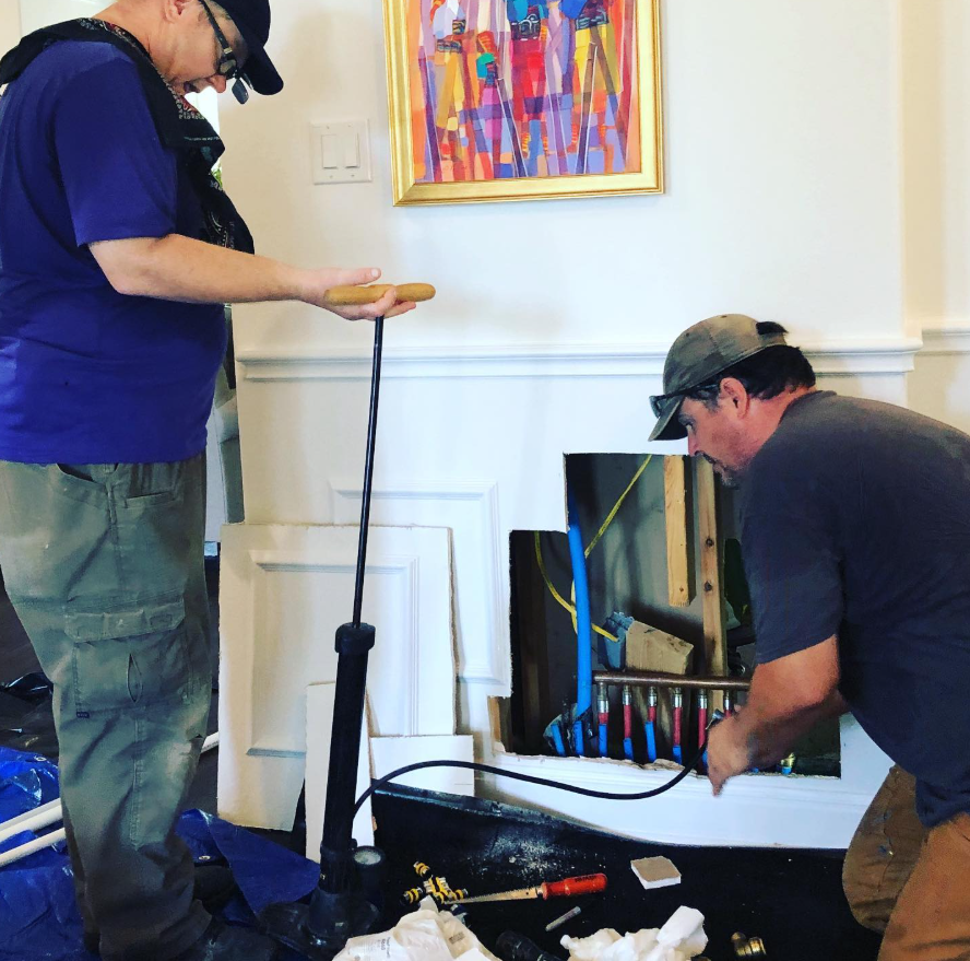 Two men assembling a piece of furniture beside a fireplace in a living room.