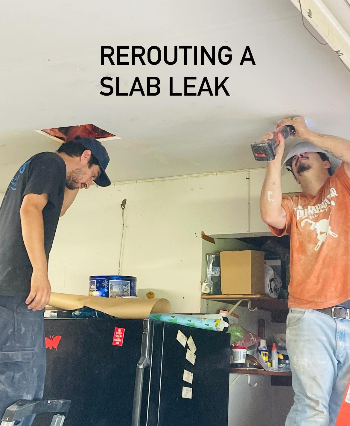 Two workers rerouting a slab leak in a kitchen ceiling, one black shirt and one orange shirt.