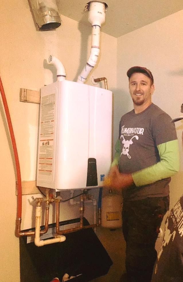 Man standing beside a white wall-mounted boiler with exposed pipes in a basement