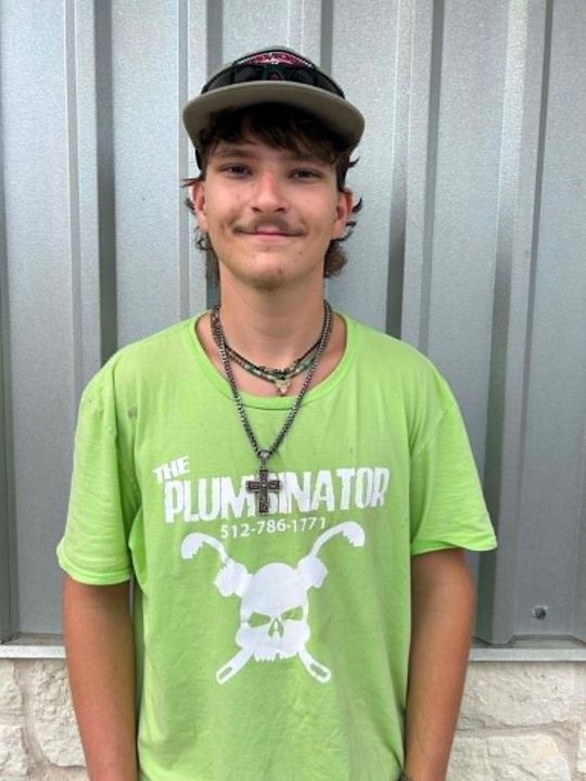 Person in a lime green T-shirt and cap standing against a corrugated metal wall.