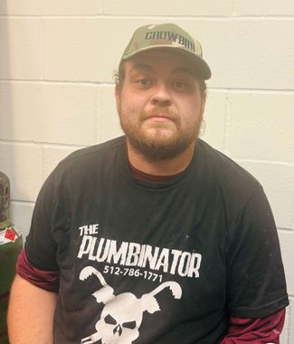 Smiling person in a neon green “The Pluminator” shirt standing before a corrugated metal wall