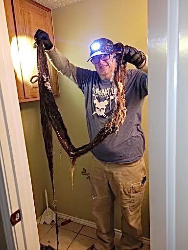 Man holding a long black snake indoors, wearing a headlamp and gloves, standing in a hallway
