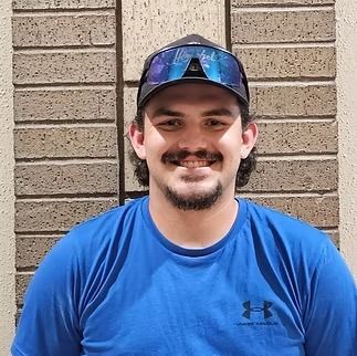 Smiling man in a blue shirt and cap standing against a brick wall