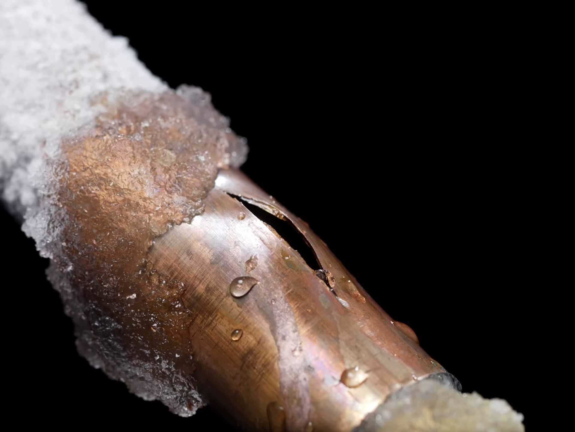 Close-up of a frosty copper pipe with water droplets against a black background