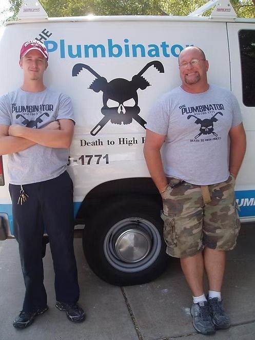 Two men in gray T-shirts stand beside a plumber van with a skull logo and
