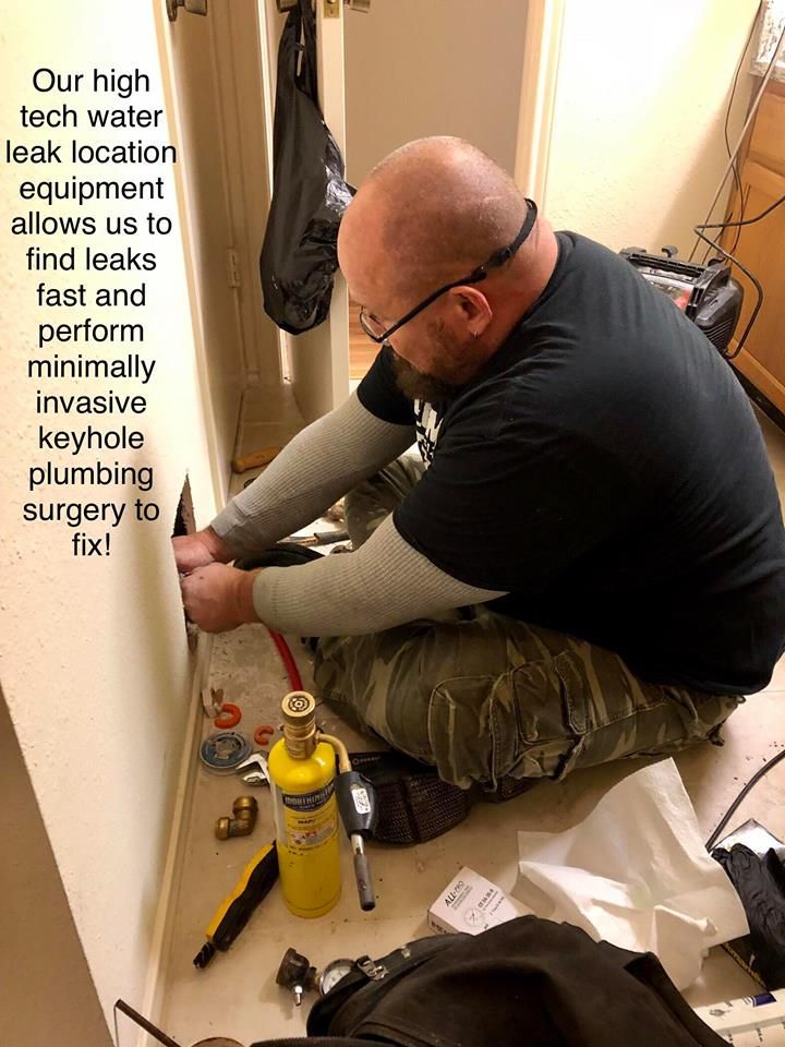 Technician installing a keyhole surge protector under a wooden floor in a hallway.