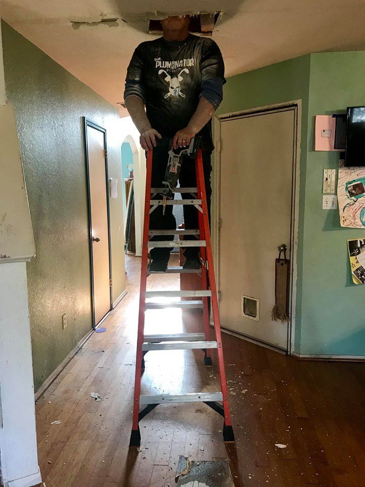 Person standing on a red ladder in a narrow hallway, working near the ceiling.