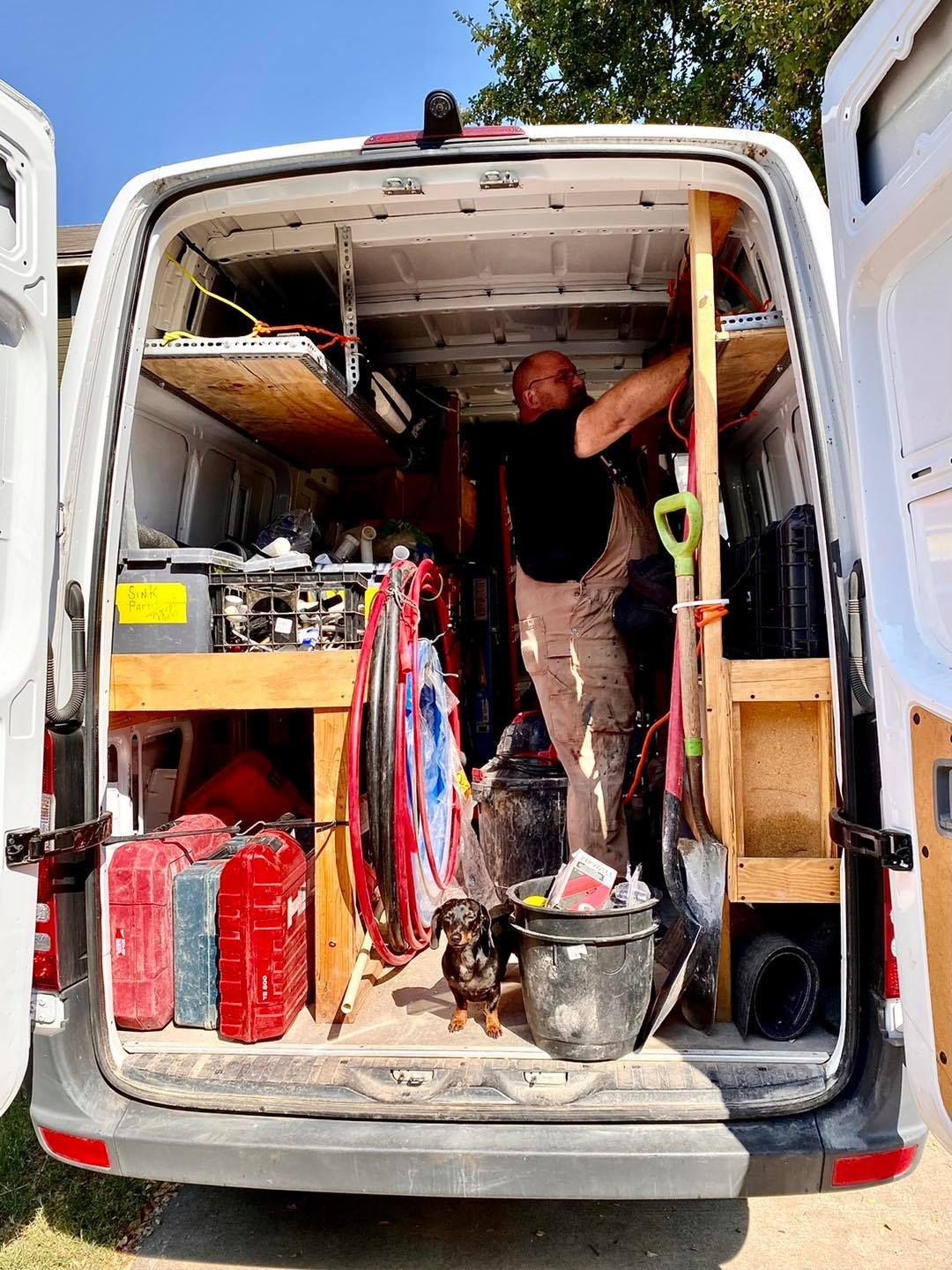 Worker standing inside an open utility van filled with tools, bins, and hoses