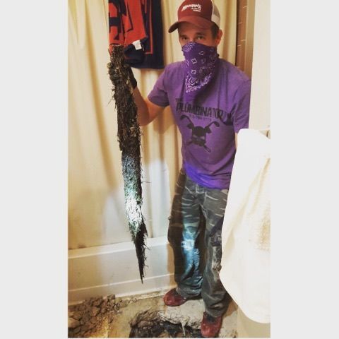 Person in a purple shirt and cap holds a large dark hanging object indoors.