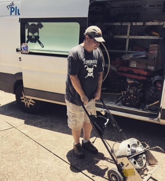 Person using a leaf blower beside a white work van with its side door open.