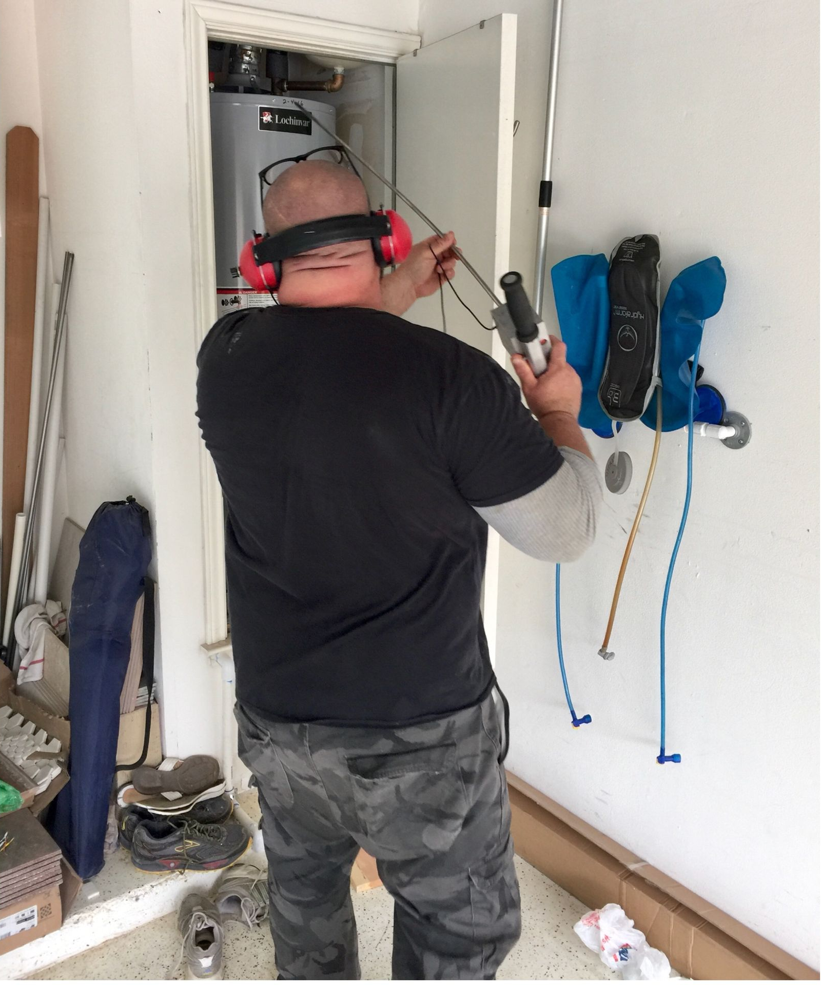 Worker using a power tool on a wall-mounted electrical panel in a narrow hallway