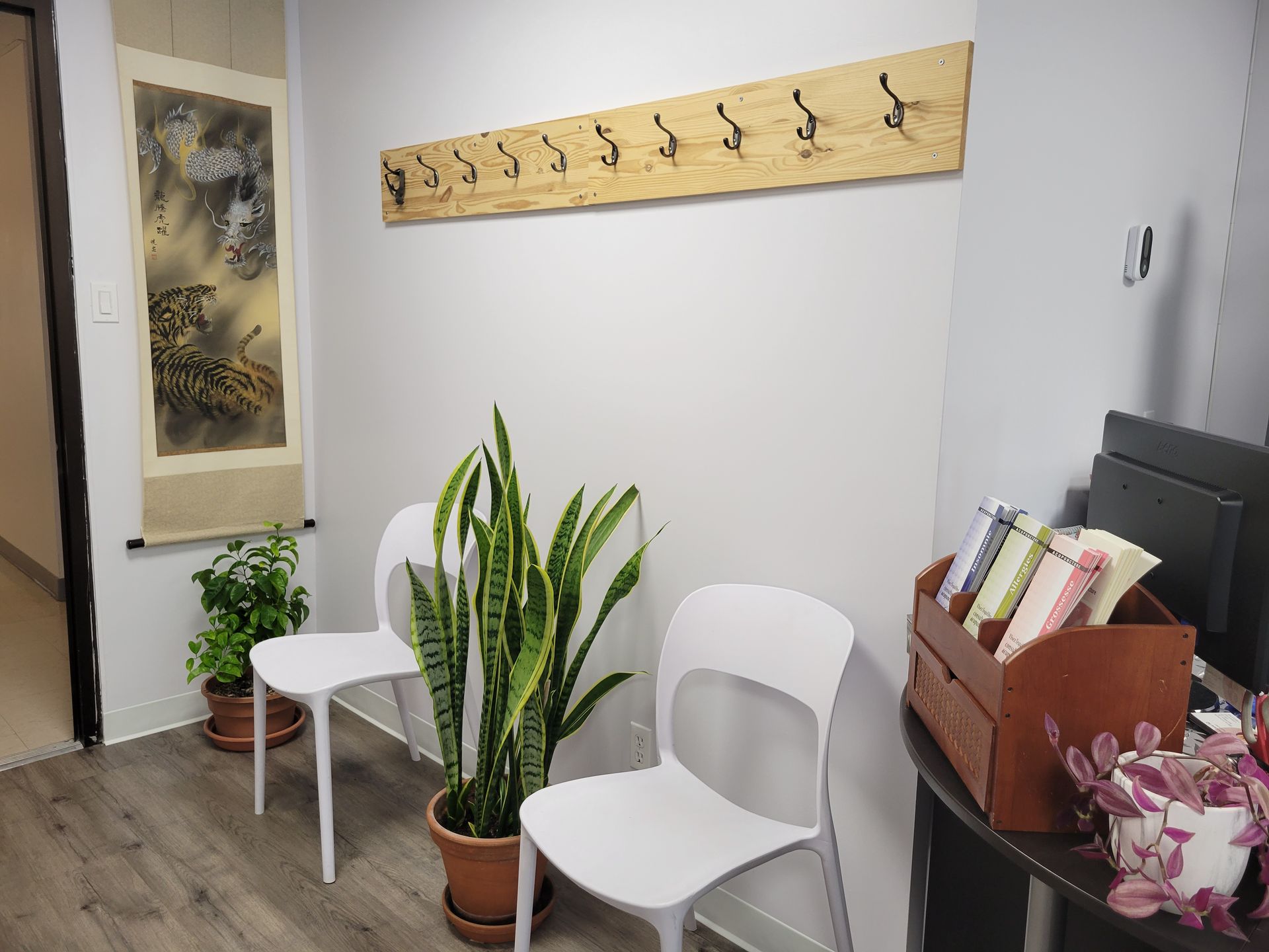 Petit espace d'attente avec chaises blanches, plantes en pot, décorations murales et porte-manteau dans un couloir