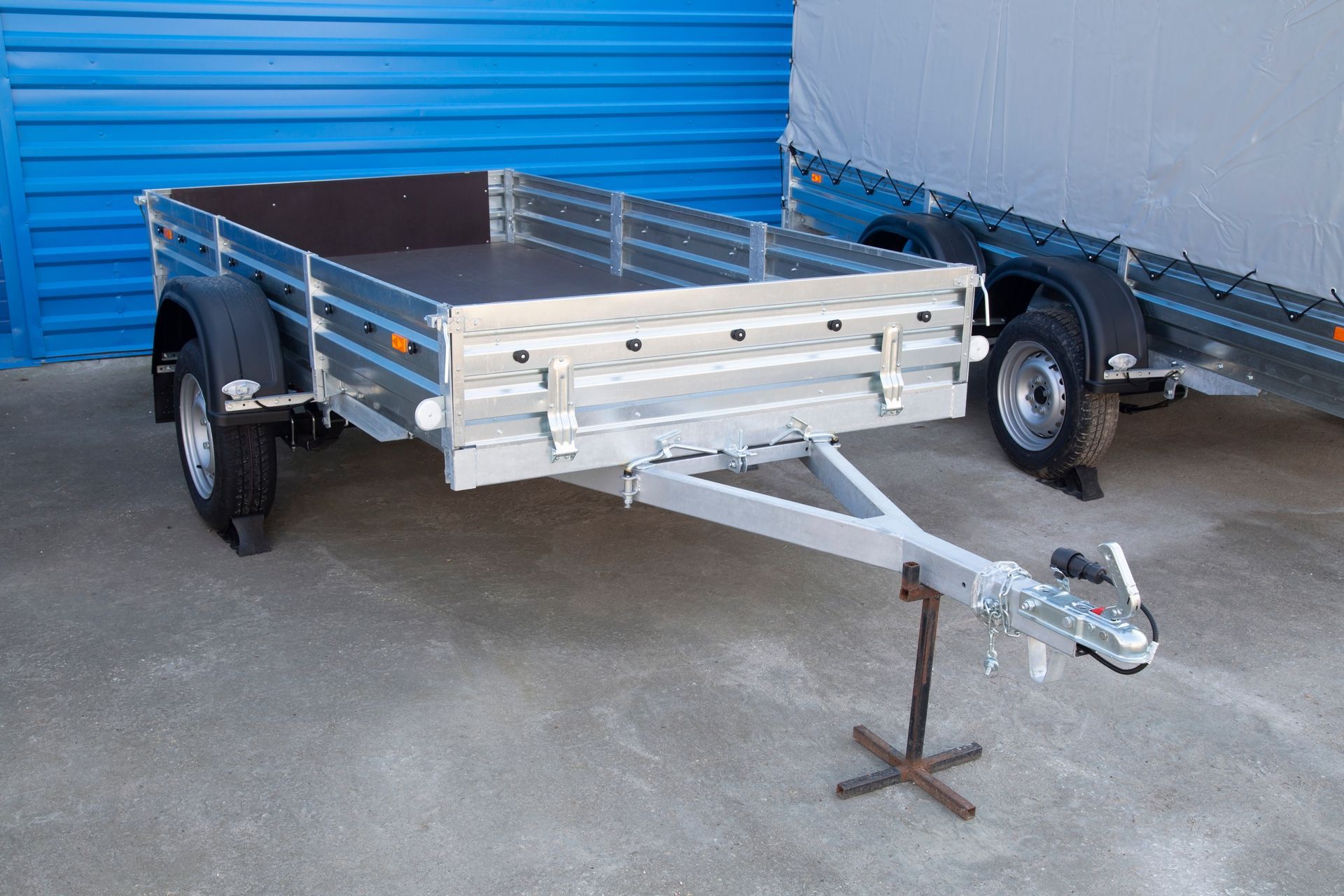 An open car trailer parked outdoors next to a cargo truck.