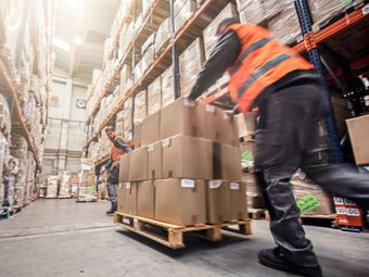 Warehouse workers in orange vests moving boxes on a pallet.