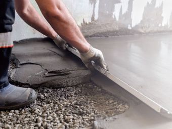 A person using a trowel to spread wet concrete on a gravel floor.