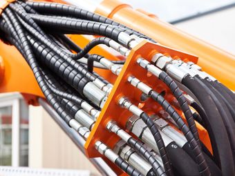 Orange construction equipment with black hydraulic hoses connected by a metal plate.