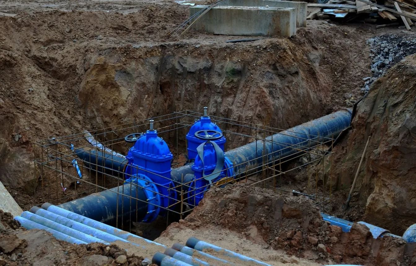 Valvola e tubi dell'acqua blu in una trincea di costruzione aperta.