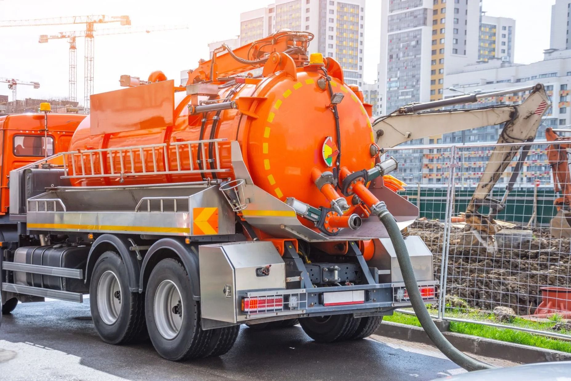 Autospurgo arancione in un cantiere edile, con il tubo flessibile esteso.
