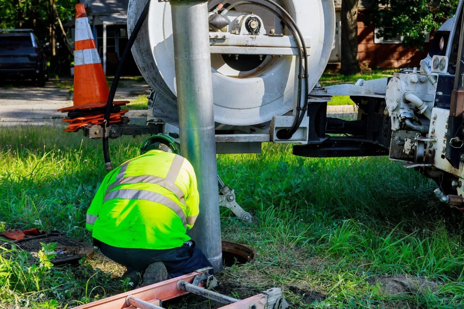 Un operaio con giubbotto catarifrangente lavora all'aperto vicino a una fogna, con un camion sullo sfondo.