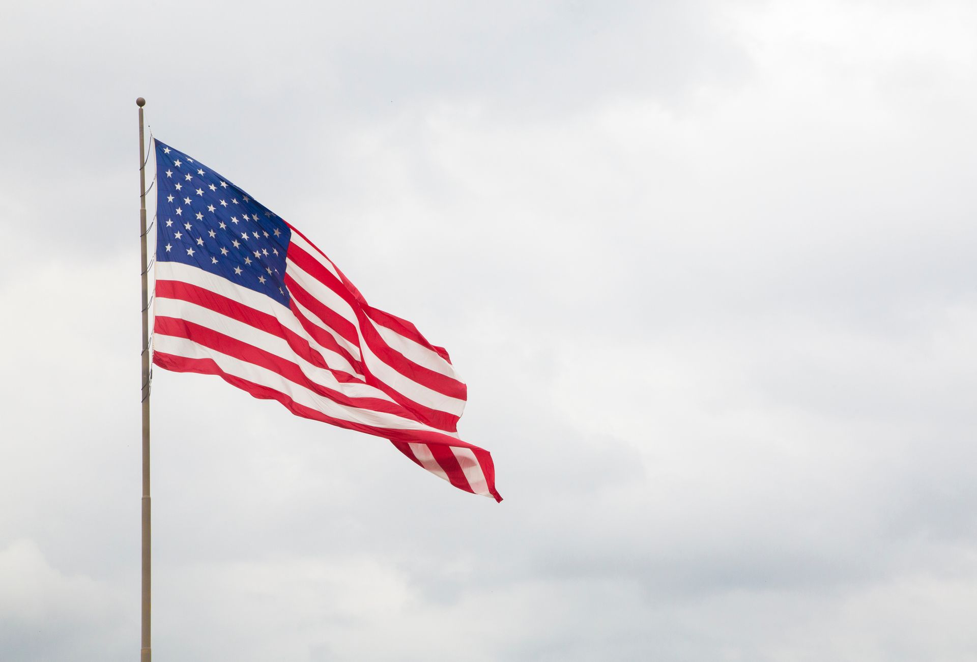American flag waving on a tall flagpole against a cloudy sky outdoors. American flag waving on a tall flagpole against a cloudy sky outdoors.