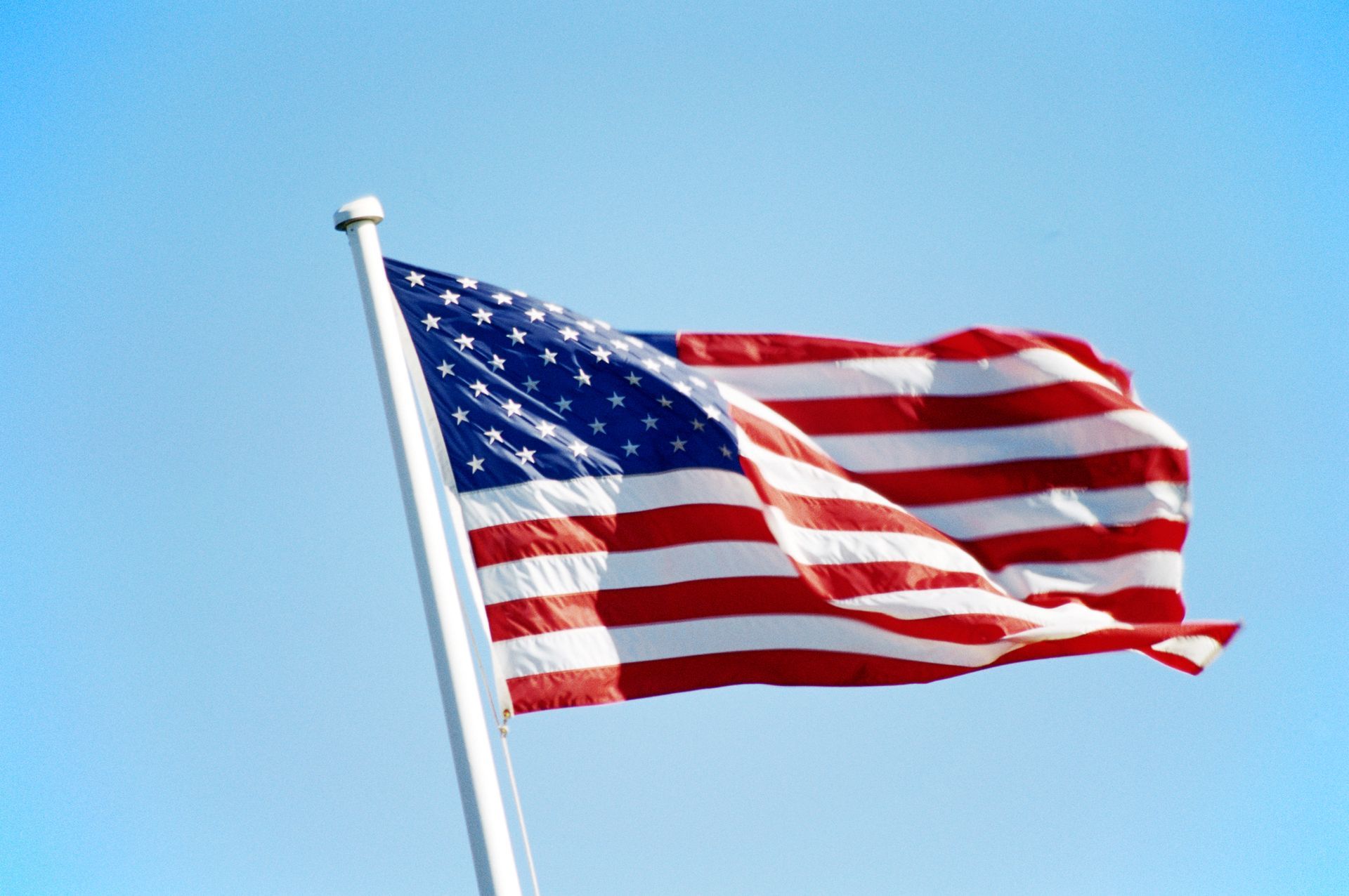 The American flag waving on a pole against a clear blue sky.