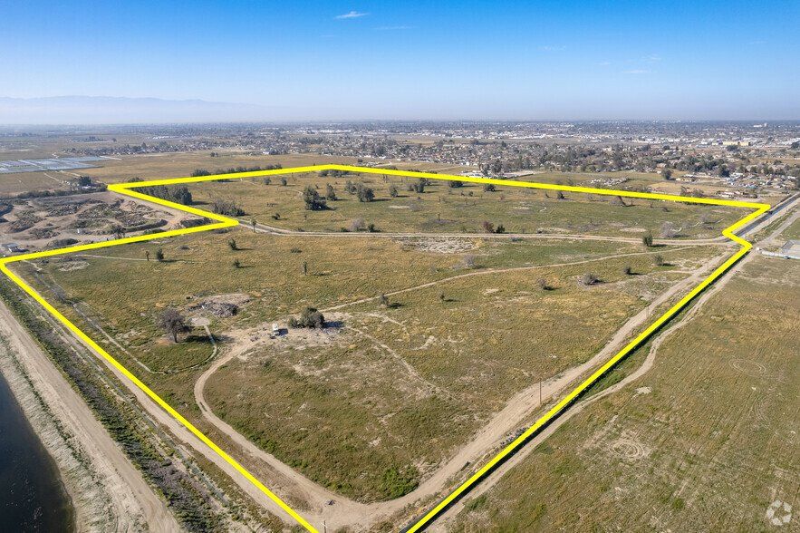 An aerial view of a large, flat, dry grassy lot outlined in bright yellow, situated near a body of water and a town.
