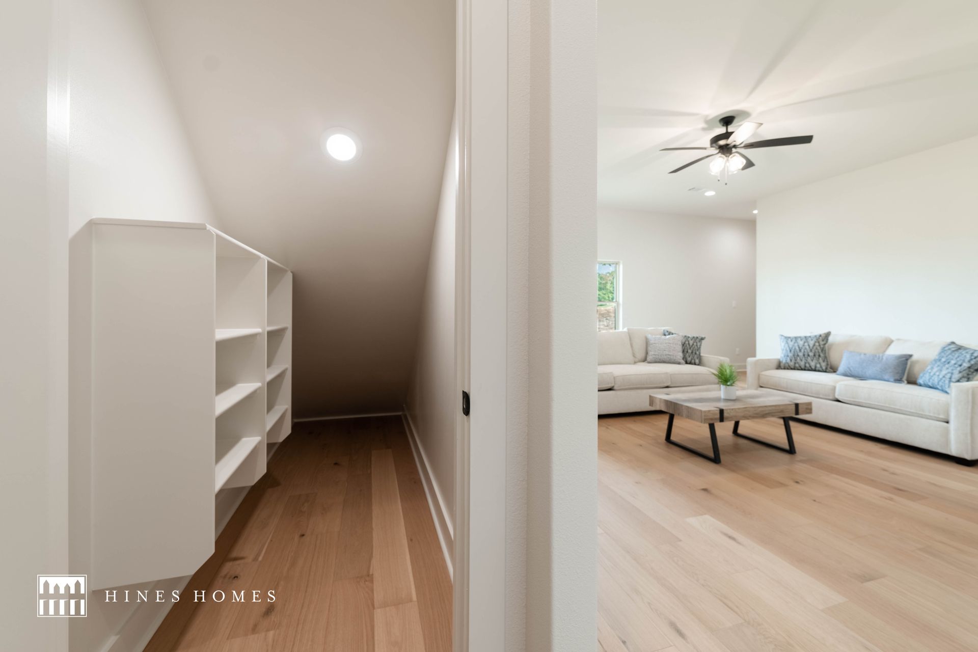 inviting bonus room with white walls, white couch that is decorated with blue pillows. the closet has big shelves 