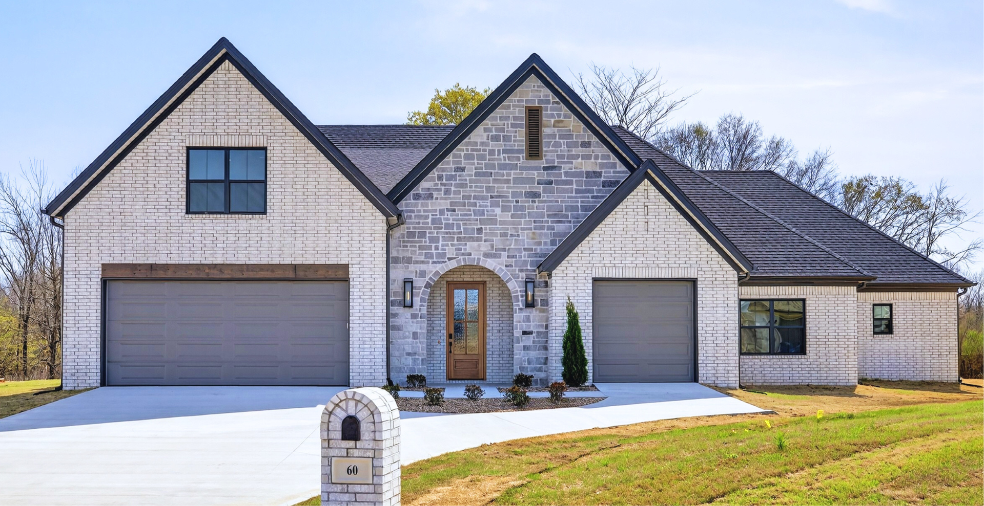 Simple custom home built by hines homes with dark brick and a white accent wall out front with a curved front porch
