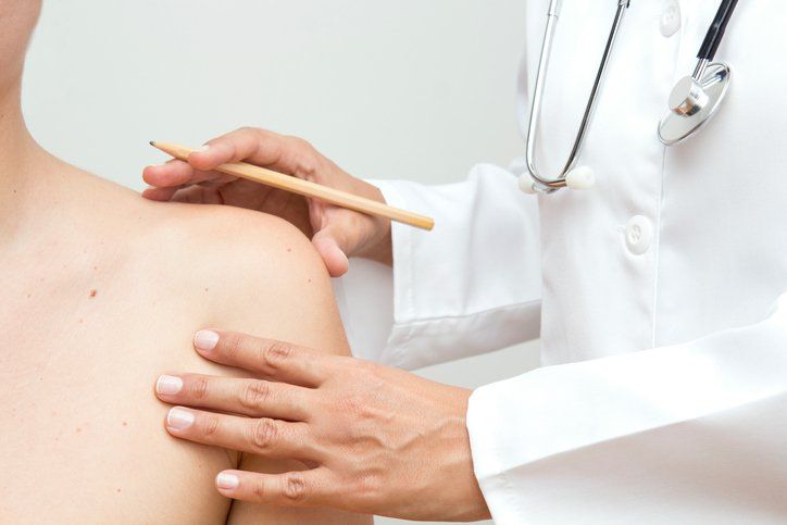 Un medico sta esaminando la spalla di un paziente con una matita.