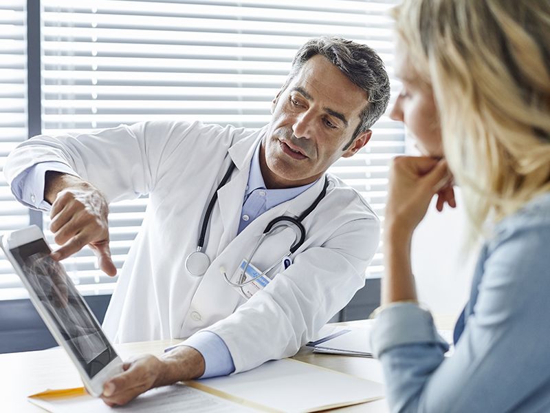 Un medico parla con un paziente mentre guarda una radiografia su un tablet.