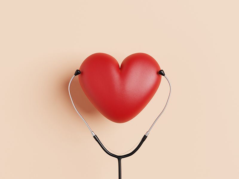 Un cuore rosso è attaccato a uno stetoscopio su uno sfondo beige.