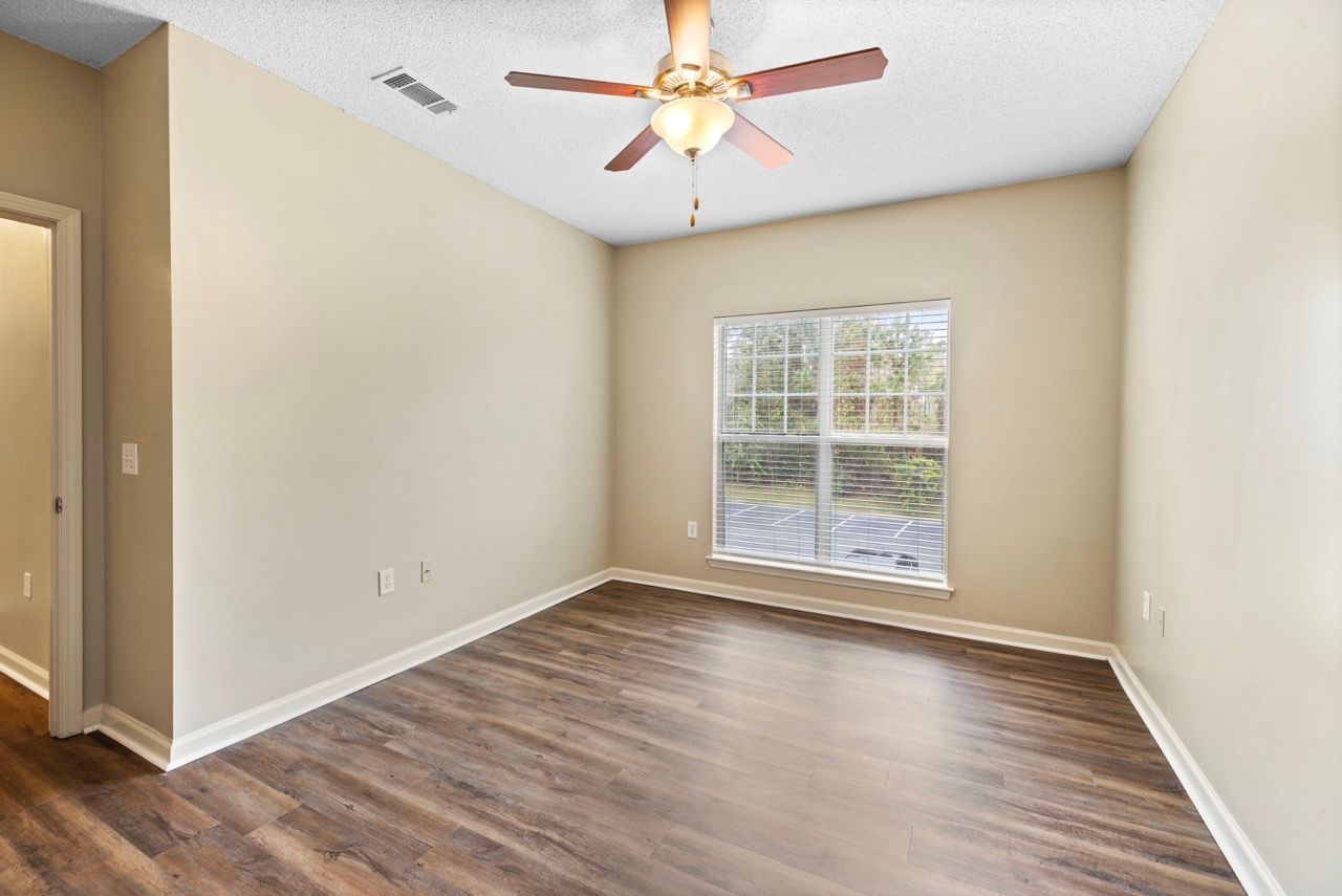 Empty beige apartment room with wood-look flooring, a window, and a ceiling fan.