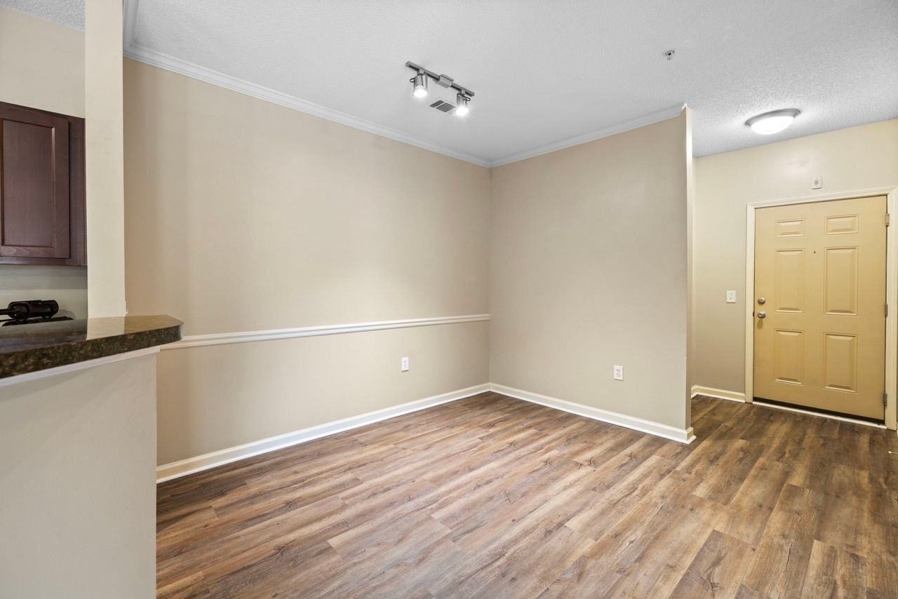 Interior of an apartment living area with beige walls, wood-look flooring, and an entry doorway.