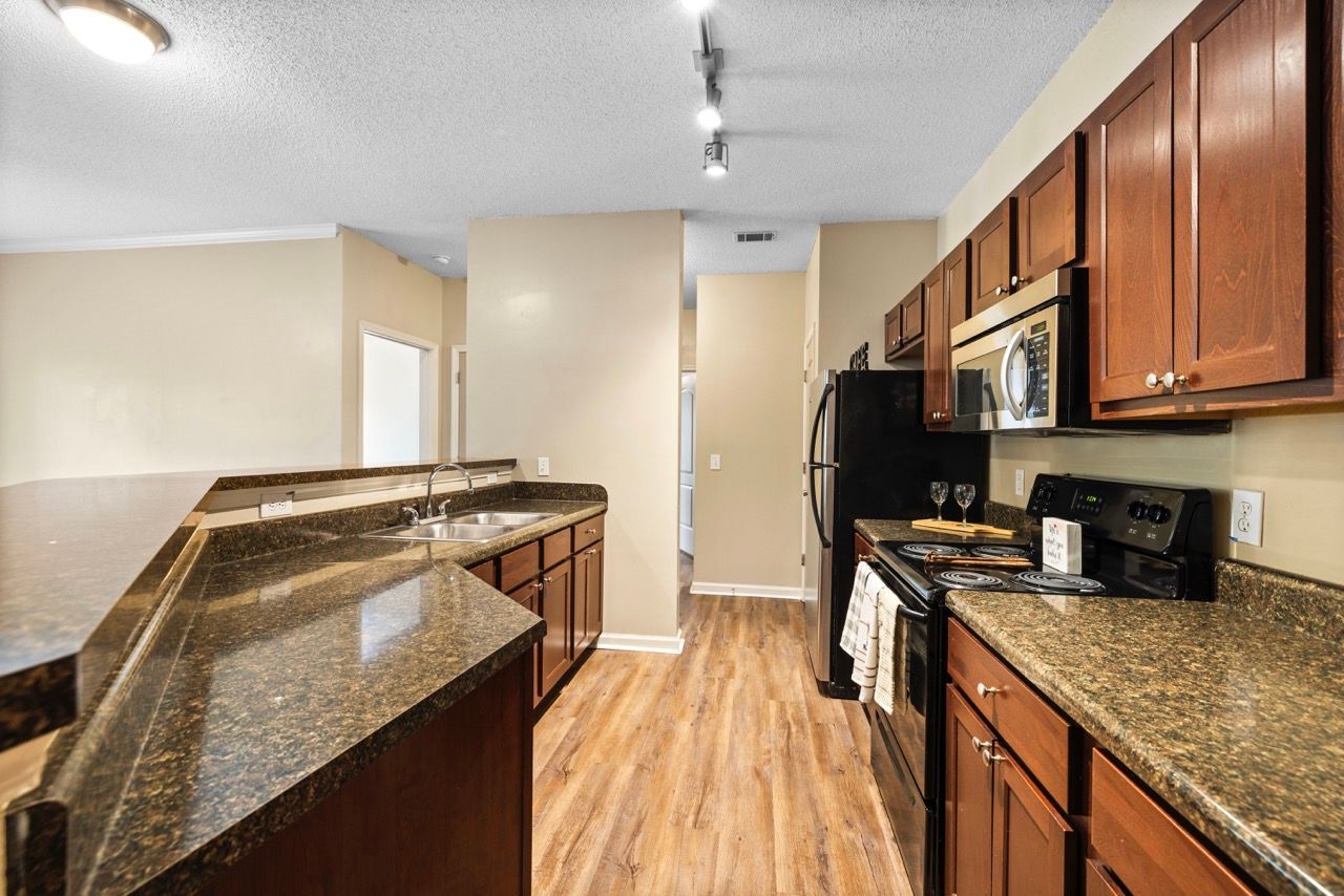 Kitchen in an apartment with granite countertops, dark wood cabinets, and stainless steel appliances.