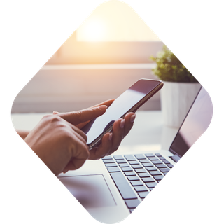 Photo of hands using a phone with a laptop also in view, all encapsulated in a diamond shape