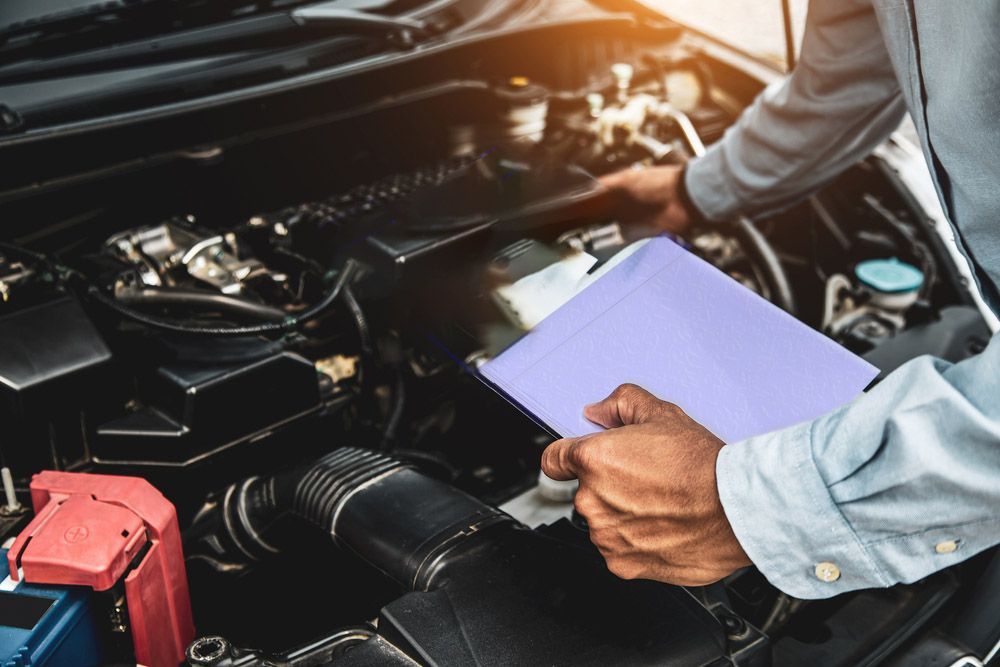 A Man Is Looking Under The Hood Of A Car While Holding A Clipboard — Valley Brake & Clutch In McDougalls Hill, NSW