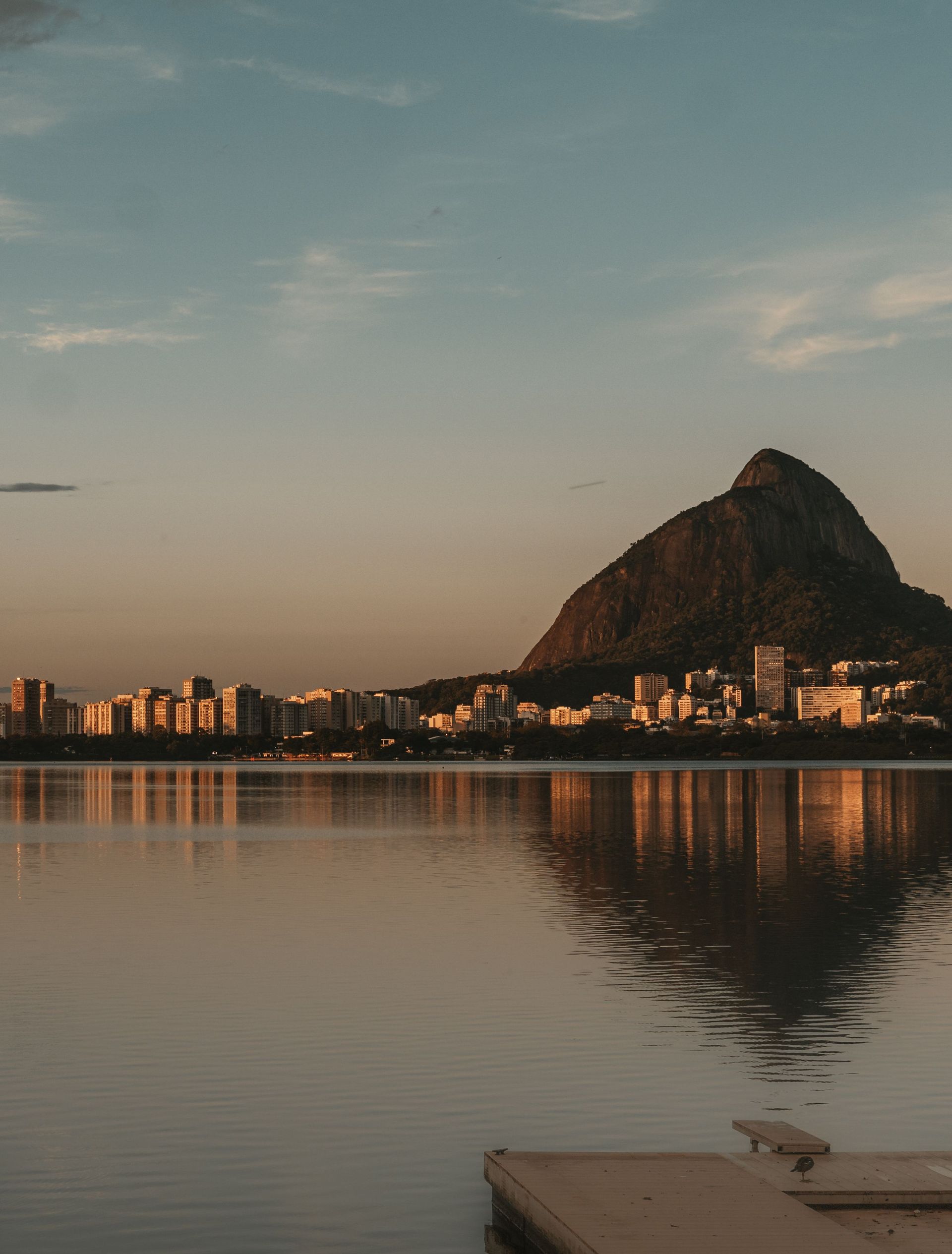 Rio de Janeiro photo with Calm waterfront at dusk with a mountain silhouette, city lights, and reflections on the water.