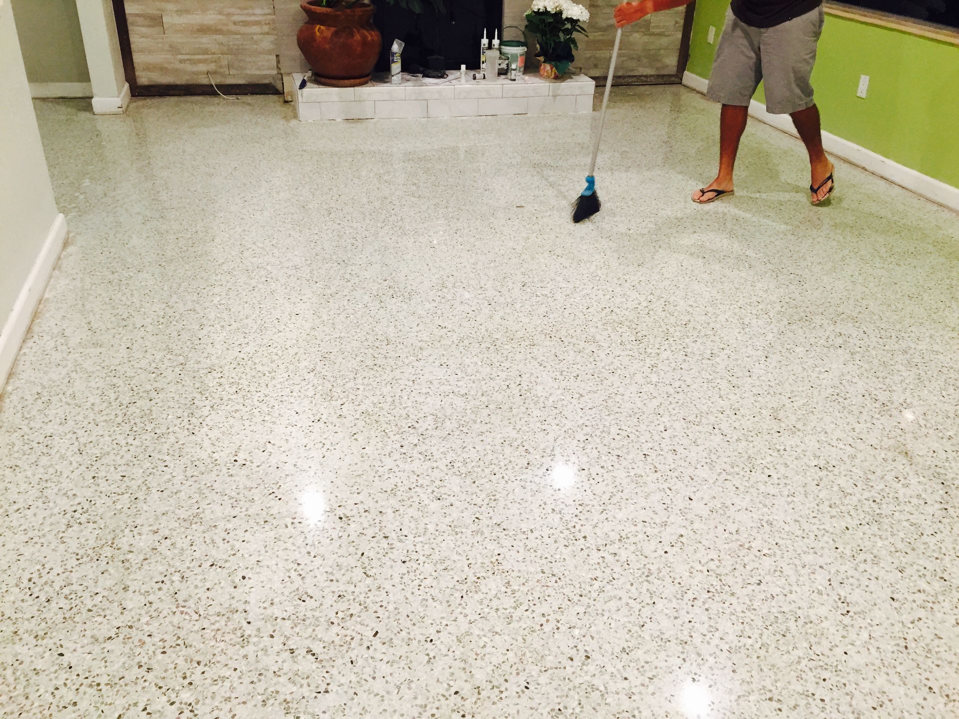 Person mopping a glossy white tiled floor in a hallway.