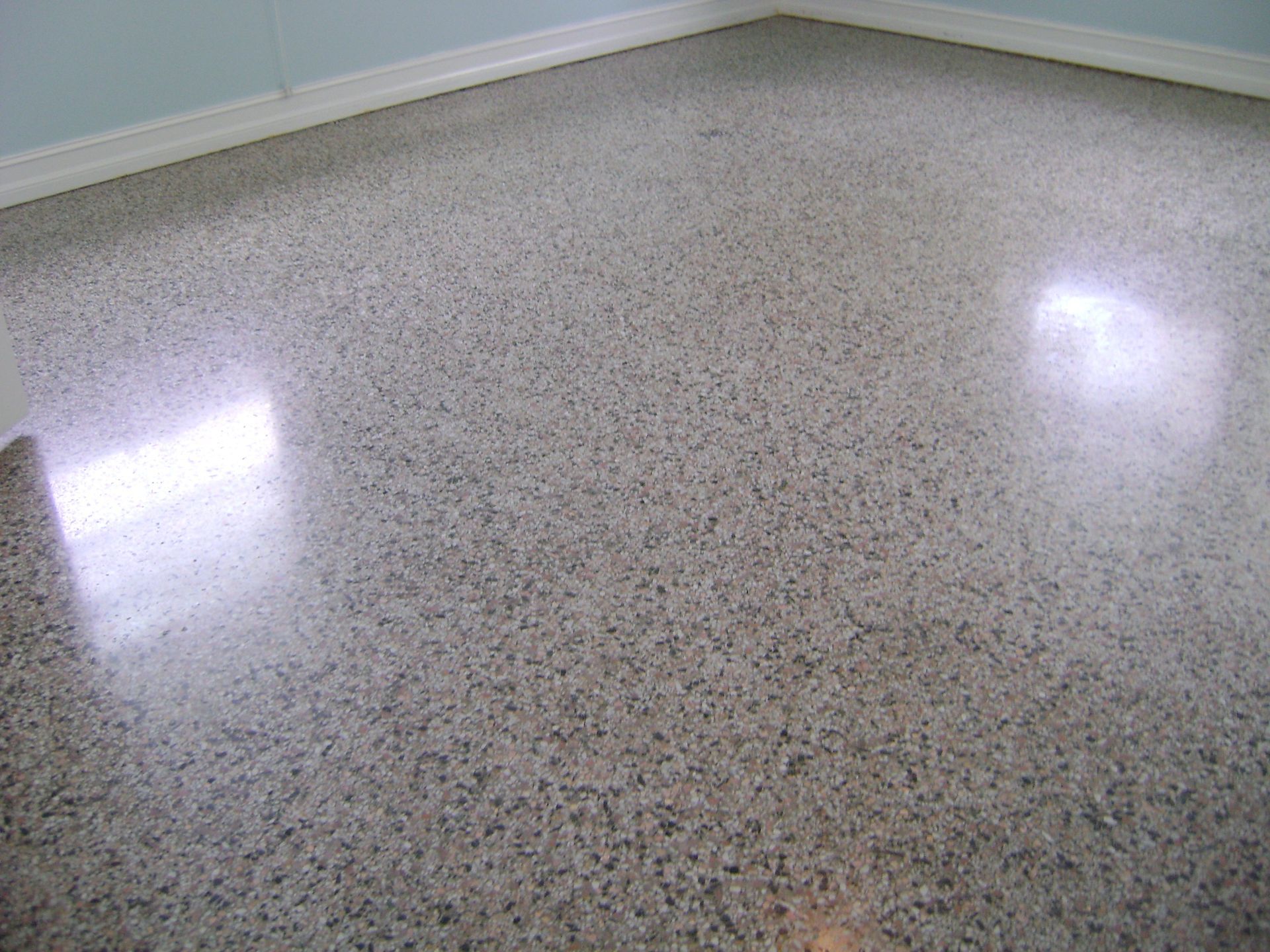 Empty speckled terrazzo floor in a room with pale blue walls and window reflections