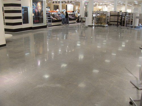Empty airport terminal with glossy floor, storefronts, and rows of chairs in the background
